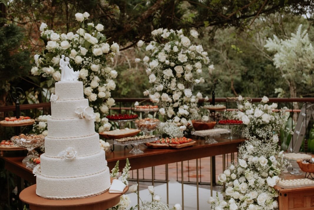 Bolo de casamento de seis andares ao lado de mesa de doces com flores brancas